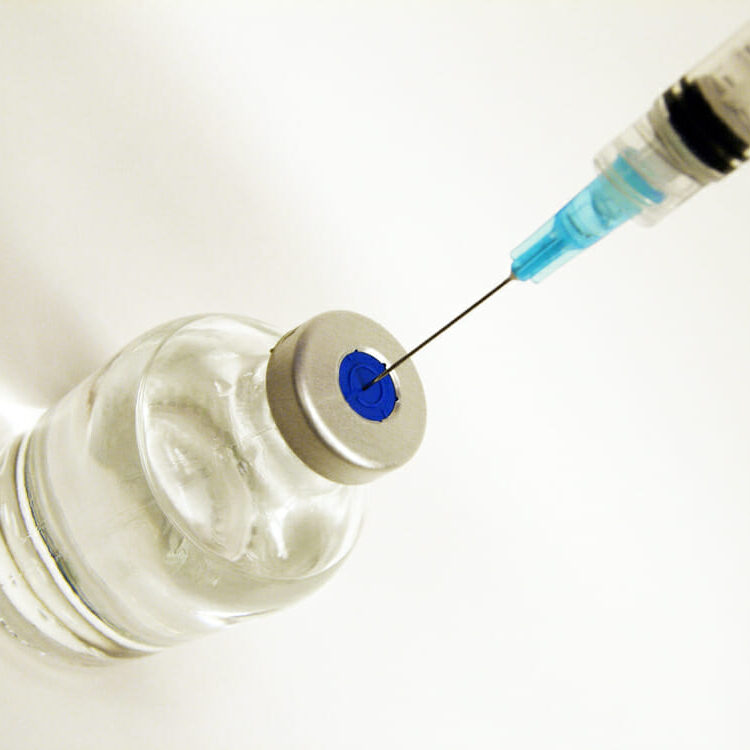 In this image: A needle goes into a vial.