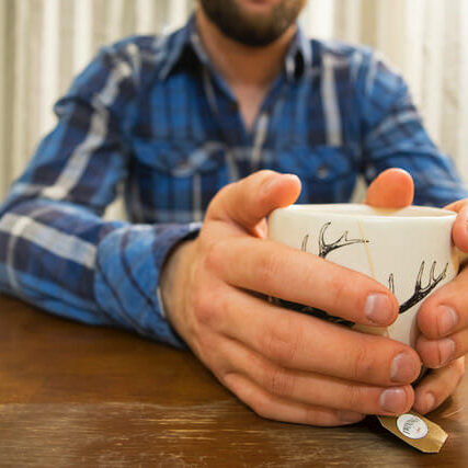 In this image: A mug rests in a man's hands.