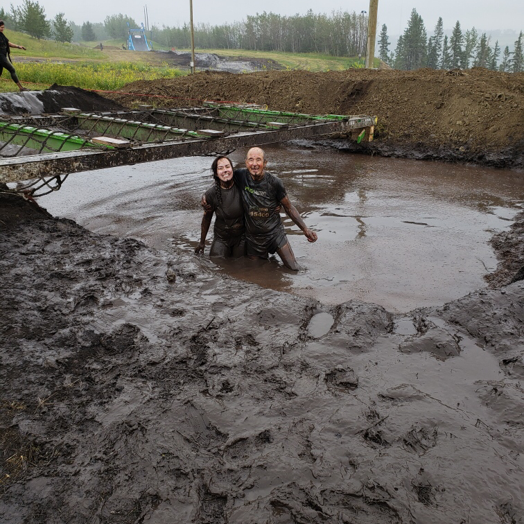 In this image: Art Noble and his granddaughter covered in mud in a hole.
