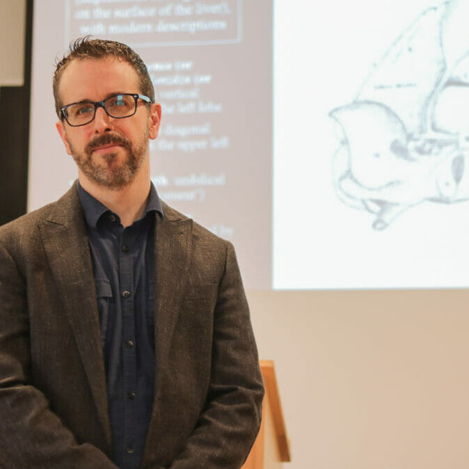 In this image: a headshot of Kyle Fraser in front of a presentation.