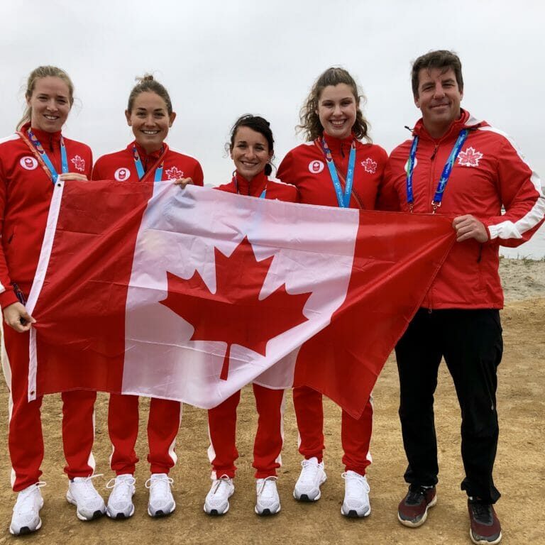 In this image: Five athletes from Team Canada pose with the Canada flag.