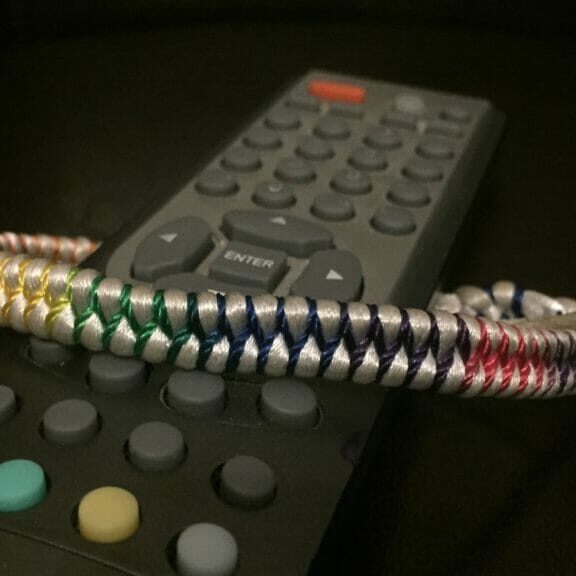 In this image: A remote control with a rainbow braclet tied around it.