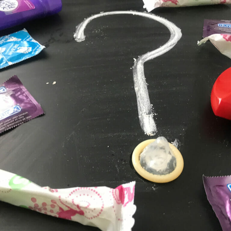 In this image: Condoms, tampons and a deodorant stick surround a question mark made with chalk.