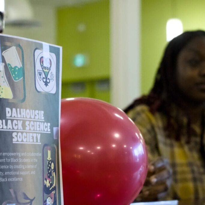 A member of the Dalhousie Black Science Society sits behind a booth at the Dalhousie Student Union’s 2025 Winter Clubs and Society Expo on Jan. 21, 2025. Image by Ferris Kerr.