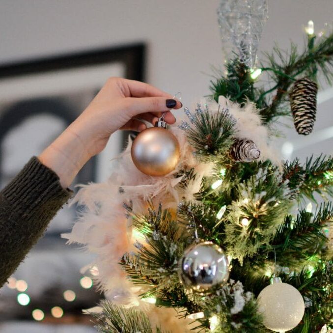 In this image: someone putting an ornament on a Christmas tree.