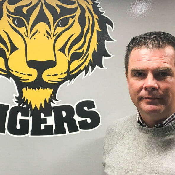 In this image: Tim Maloney beside a Dal Tigers logo.