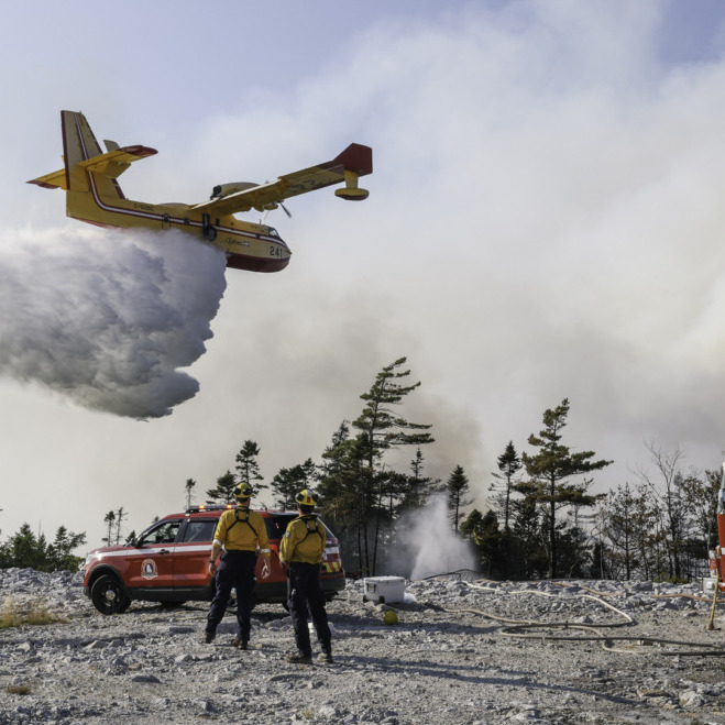 Department of Natural Resources firefighters Dylan Mulder, left, and Elijah DeCoste, both of Jeddore, watch a water bomber make a pass over the wildfire. (Image by Province of Nova Scotia)