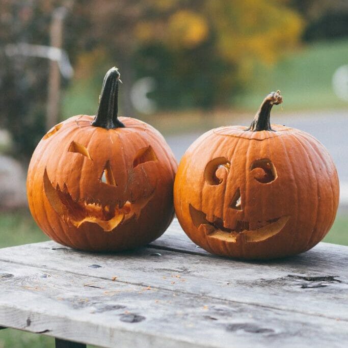 Two unlit jack-o-lanterns on a wooden table.