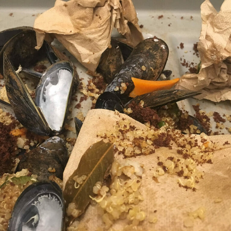 In this image: A bin of leftover quinoa, mussel shells, napkins and other food waste.