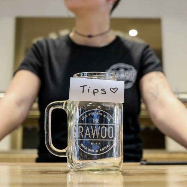In this image: A Grawood employee stands behind an empty tip jar.